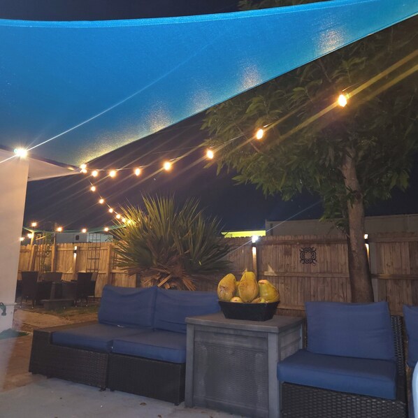 An outdoor seating area with a blue canopy, string lights, and a table with a fruit bowl. - 10 minutes to the beach, Cozy Family Stay · Near everything · Free Parking (Oakland Park)