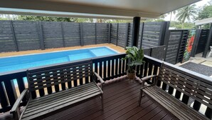 Un espacio al aire libre cubierto con piscina, terraza de madera y barandillas de metal negro.