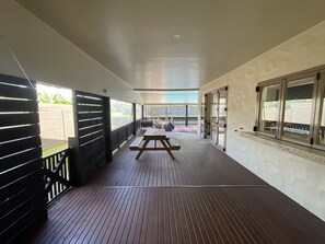 Un espacio al aire libre techado con terraza de madera, una mesa de picnic y vistas al jardín a través de amplios ventanales.