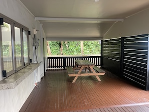 A covered patio with a wooden table and benches, a view of greenery, and a black fence. - Villa Honey Rose Private Pool & unlimited WIFI (Rarotonga)