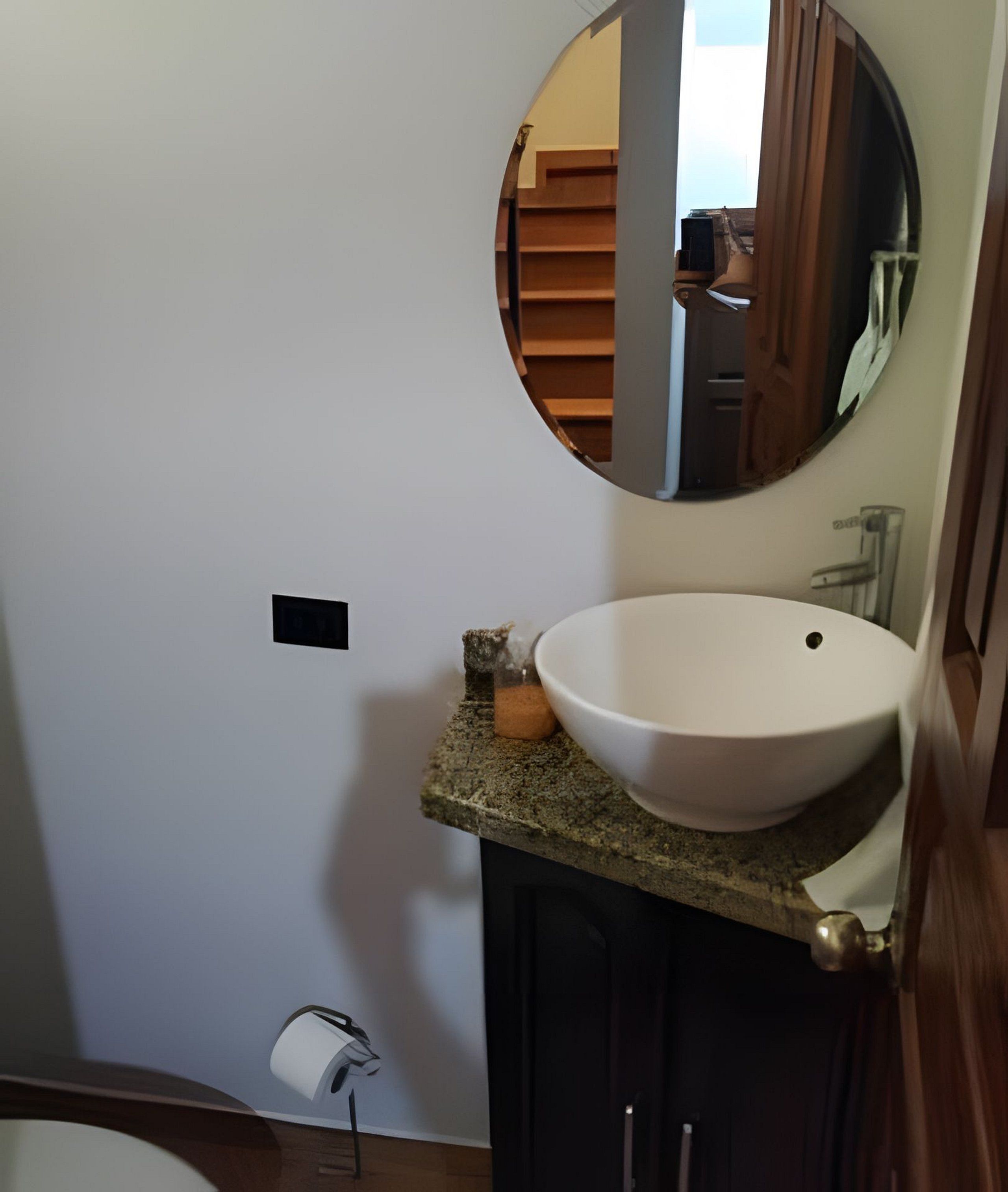 Un baño con un espejo redondo, un lavamanos blanco y un inodoro.