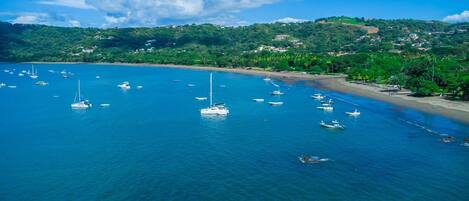 A coastal area with boats on the water, a beach, and hills in the background.