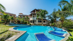 Una gran piscina al aire libre con varias zonas de descanso, rodeada de palmeras y un edificio de varios pisos.