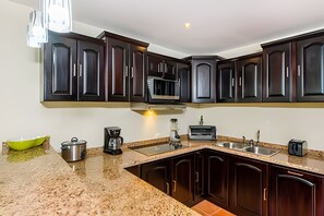 A kitchen with dark wood cabinets, a granite countertop, a built-in microwave, a coffee maker, and a toaster. - Coco Sunset Hills 52 (Coco)