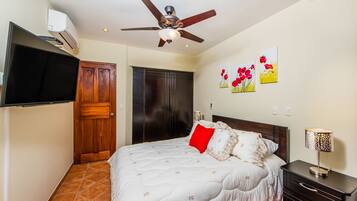 A bedroom with a bed, a ceiling fan, a TV, a wardrobe, and artwork on the wall.