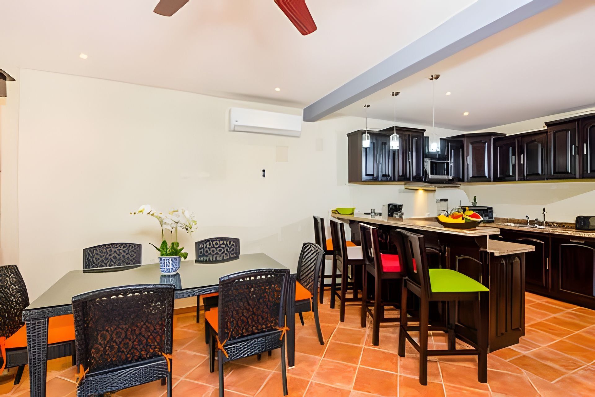 A dining area with a table and chairs, a kitchen with dark cabinets, and a ceiling fan.
