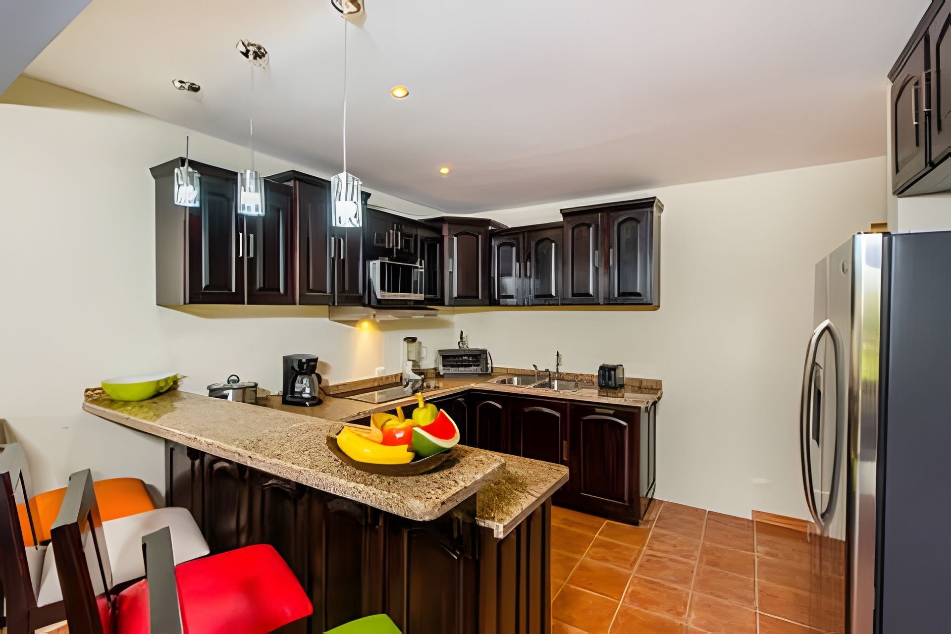A modern kitchen with dark cabinets, a granite countertop, a built-in microwave, a coffee maker, and a fruit bowl.