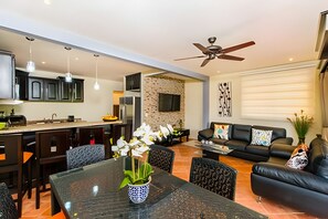 Eine moderne Küche mit Essbereich, ein Wohnzimmer mit Sofa und Fernseher sowie ein Deckenventilator.