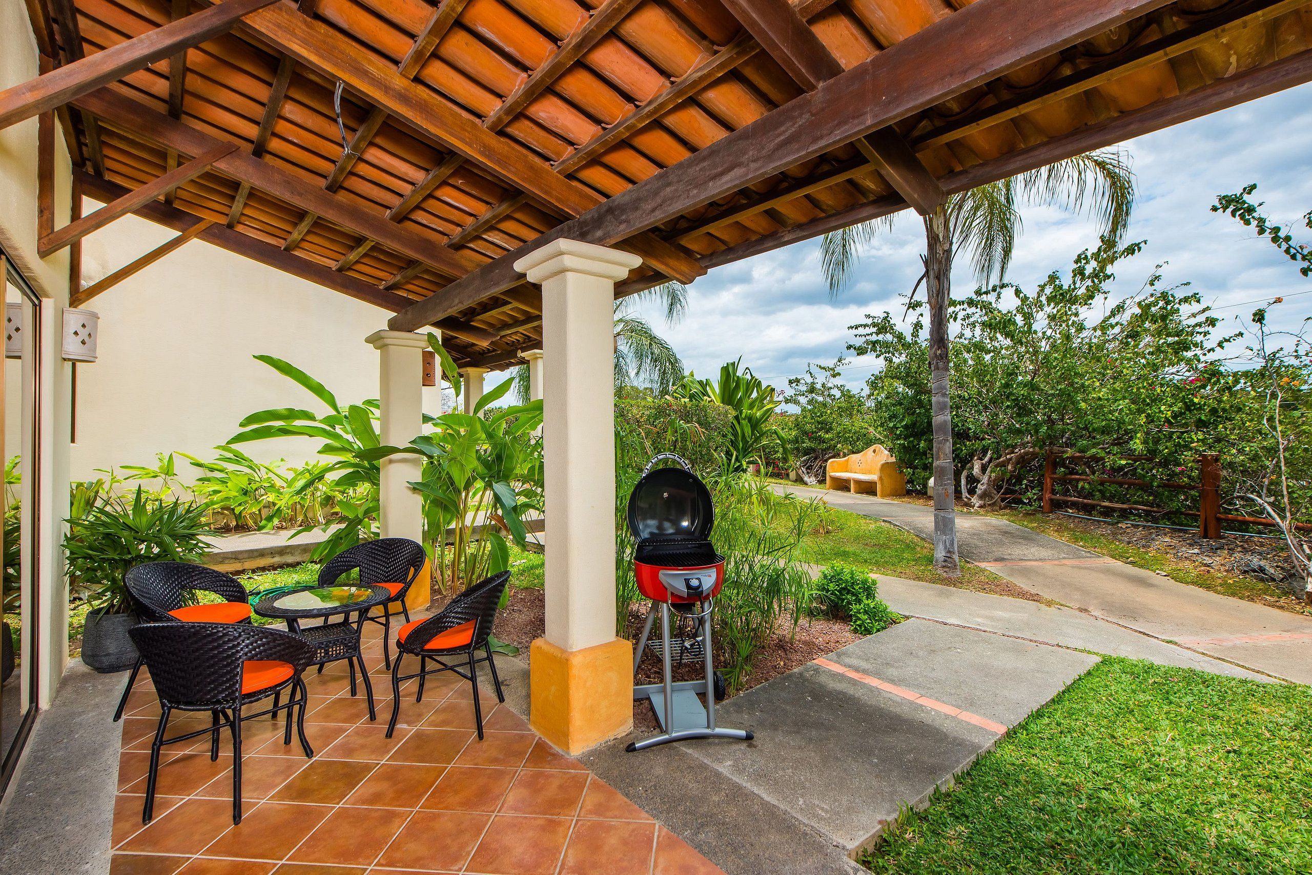An outdoor patio with a grill, chairs, and a covered area with a tiled floor.