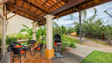 An outdoor patio with a grill, chairs, and a covered area with a tiled floor.