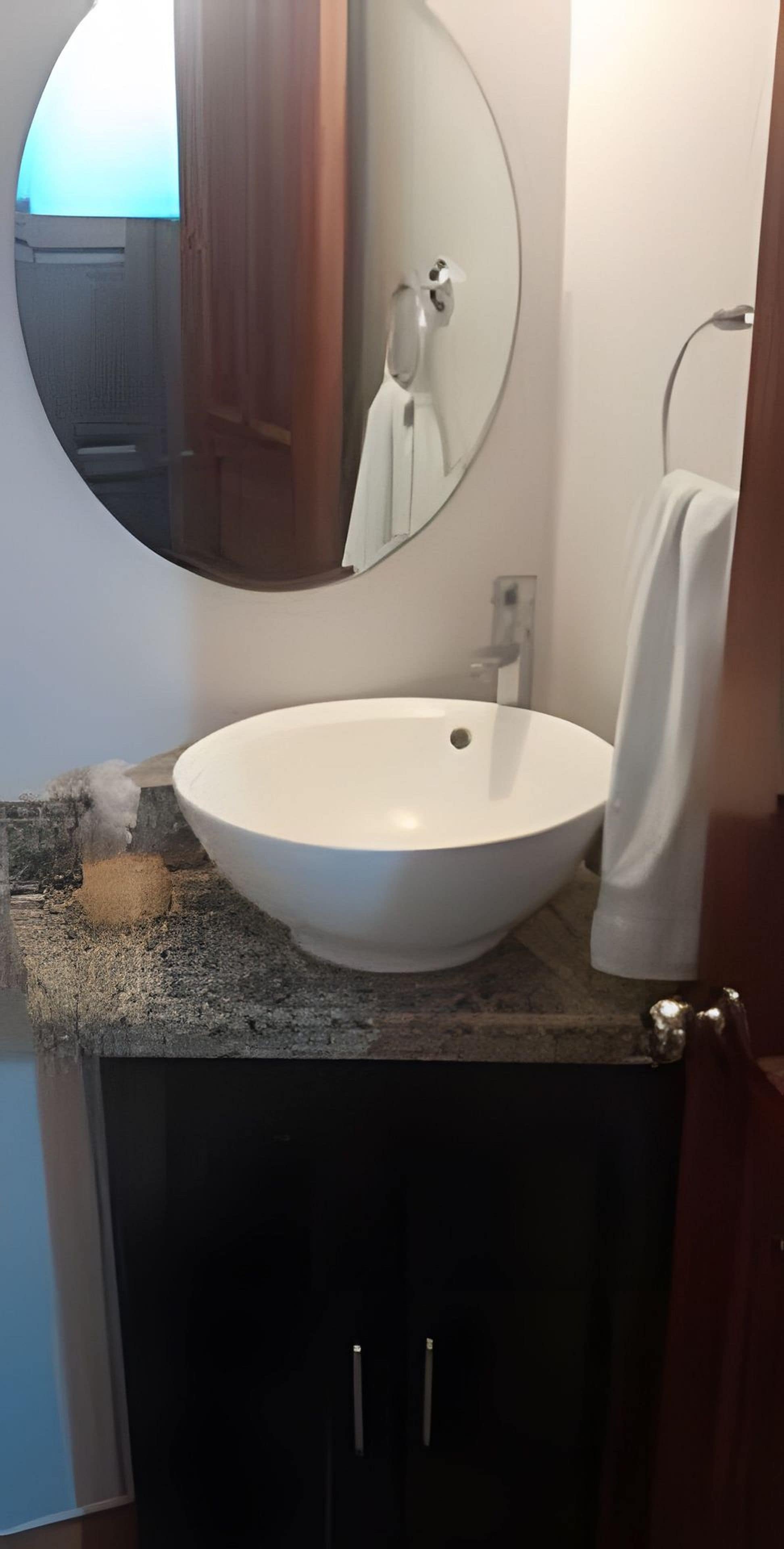 A bathroom with a round mirror, a white sink, and dark cabinets.