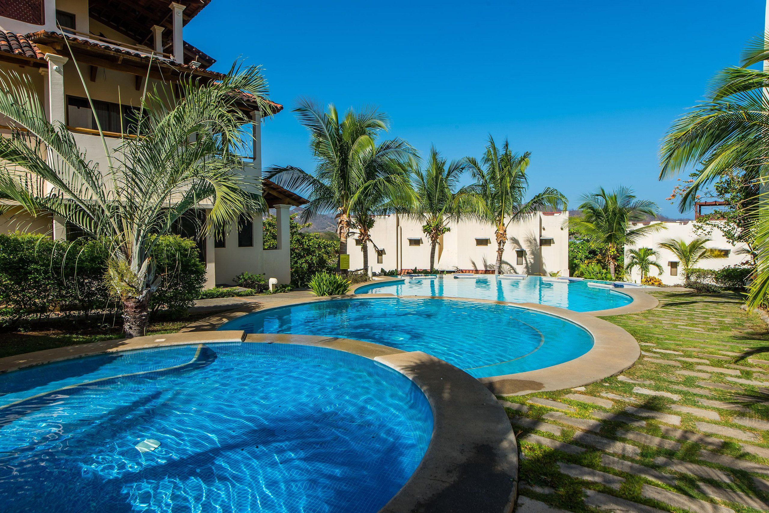 A resort with multiple swimming pools, palm trees, and a clear blue sky.