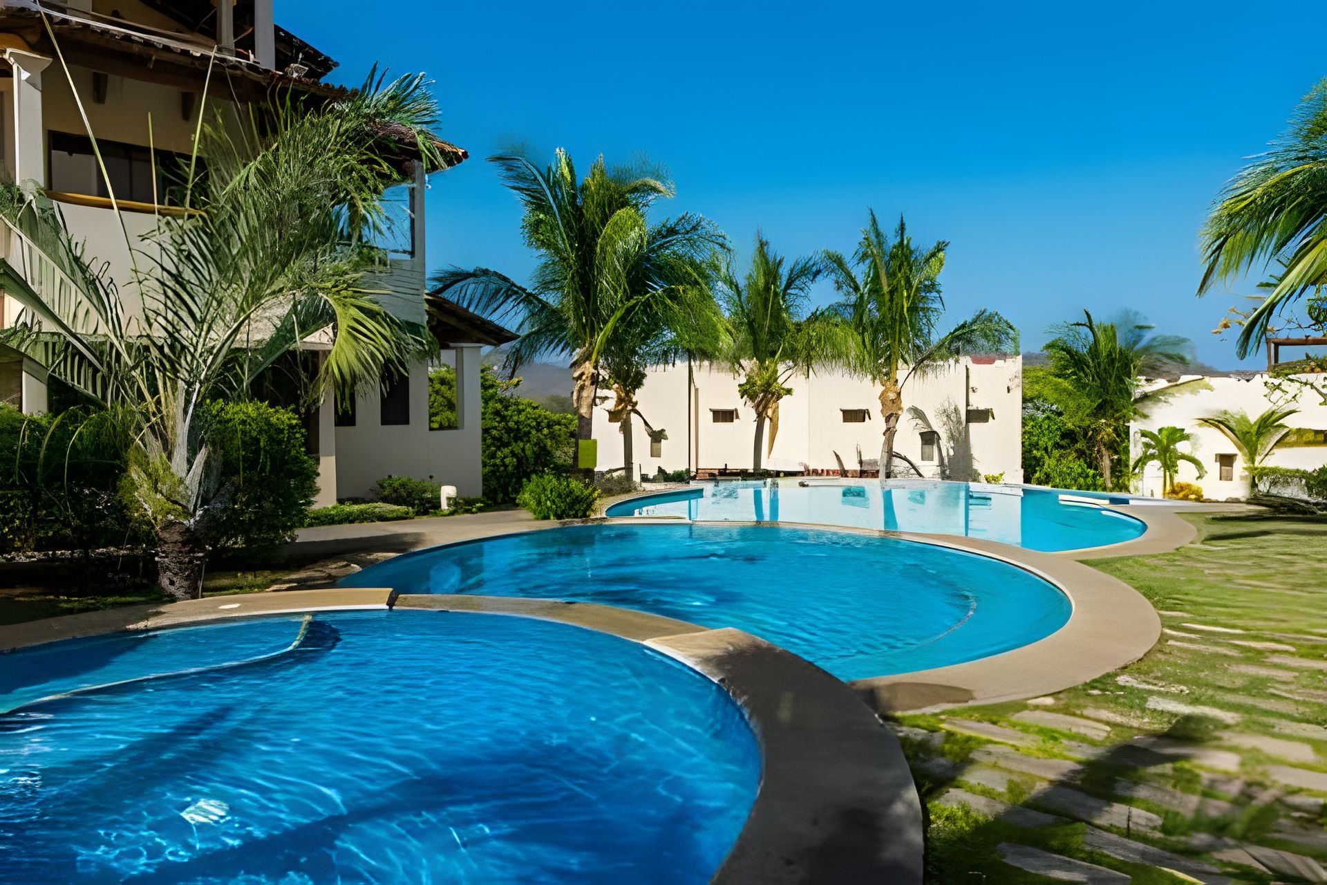 Ein Resort mit mehreren Pools, Palmen und blauem Himmel.