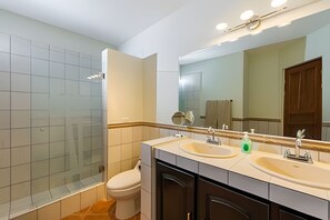 Un baño moderno con cabina de ducha de vidrio, inodoro, lavabo con espejo y tocador.