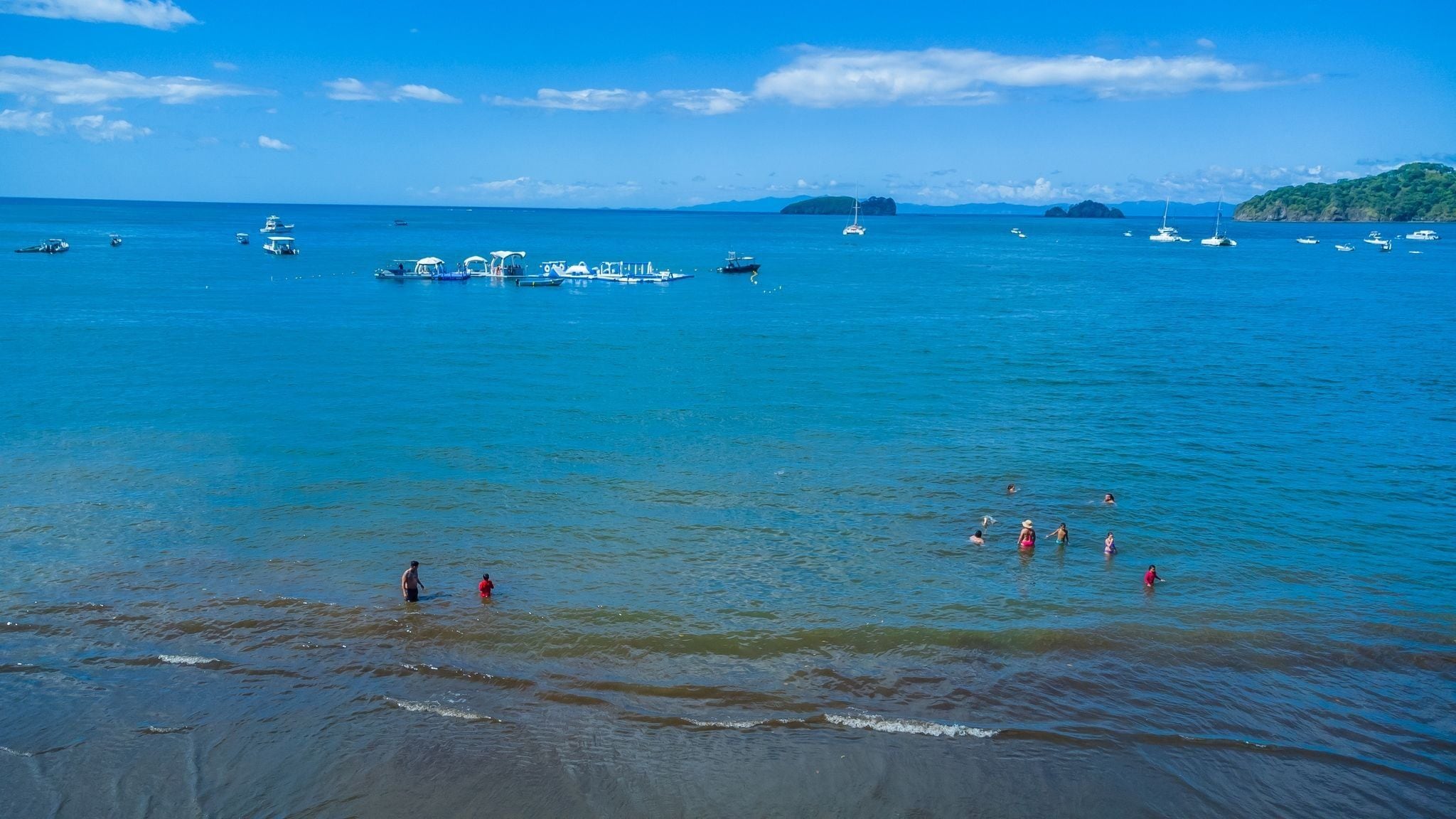 Une scène côtière avec des bateaux et des personnes dans l’eau.