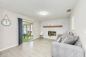 Relax in this inviting living room with a fireplace, sofa, and sliding glass door leading to a serene outdoor space.