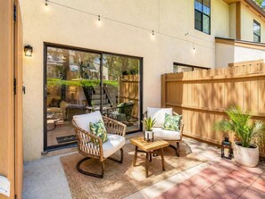 Un patio con sillas de mimbre, una pequeña mesa y una valla de madera.