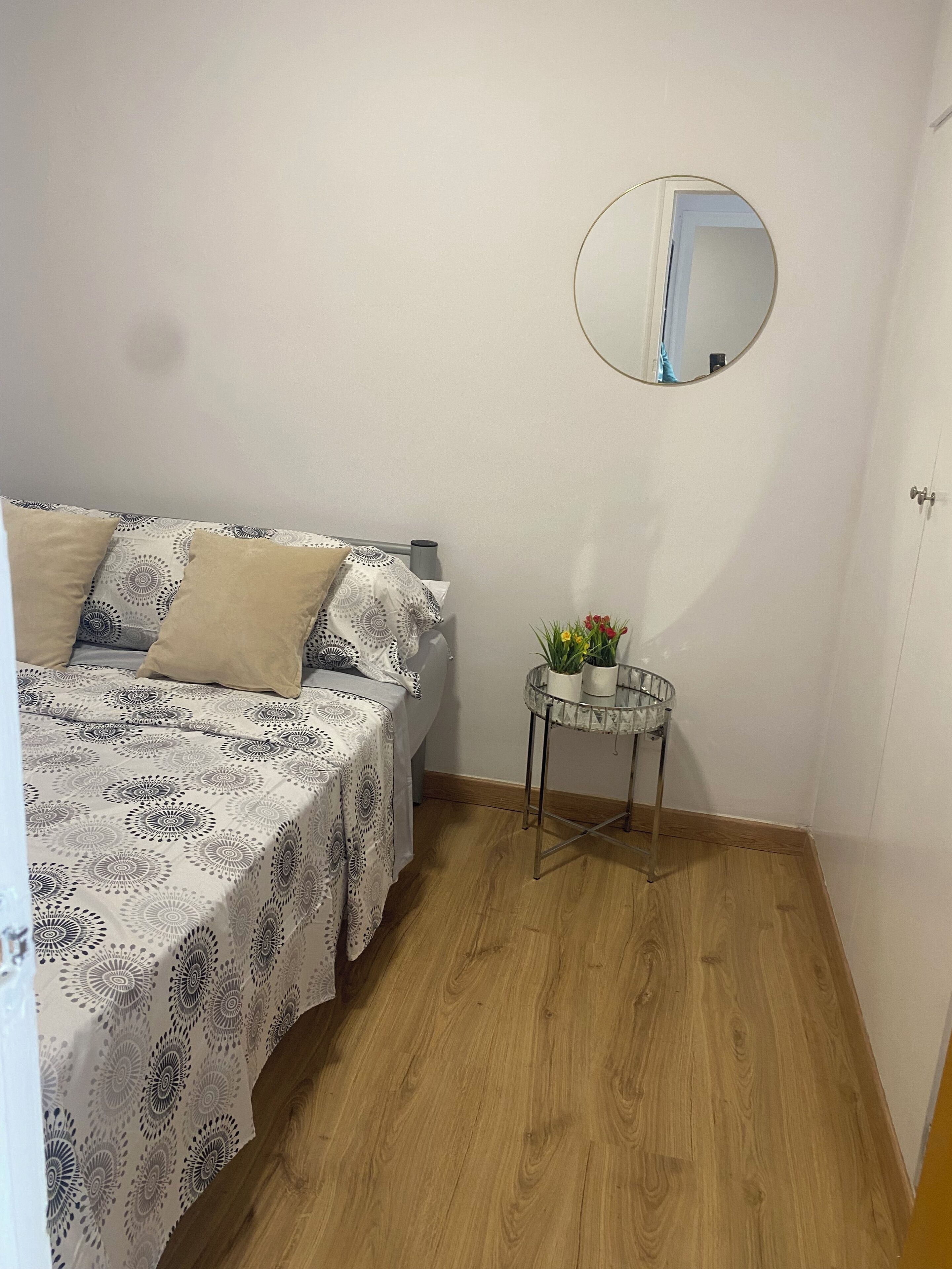 A bedroom with a bed, a bedside table with a mirror, and a small potted plant.