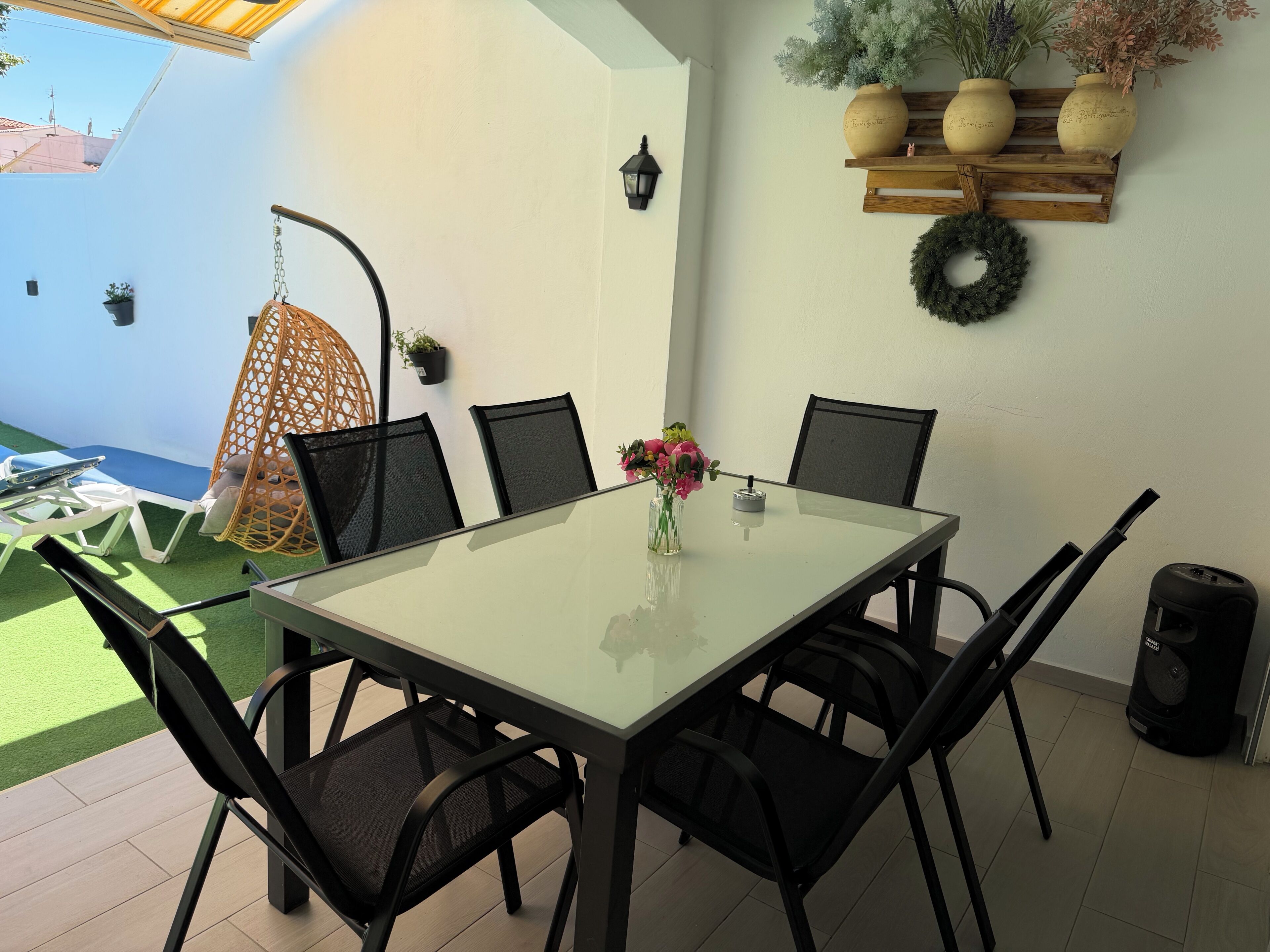 Un comedor con mesa de vidrio, sillas negras, una silla colgante y plantas en macetas.