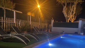 Une piscine dont le bord est recouvert de carreaux, entourée d’une clôture et agrémentée de plantes en pot.