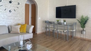 Un salon moderne comprenant un canapé, une table basse, une table à manger avec des chaises, un téléviseur fixé au mur et une plante en pot.