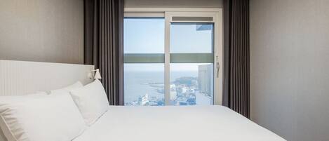 Quarto de hotel com cama, janela com cortinas e vista para a paisagem urbana.