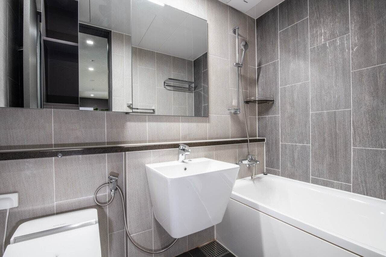 A modern bathroom with a white sink, a bathtub, and a large mirror.