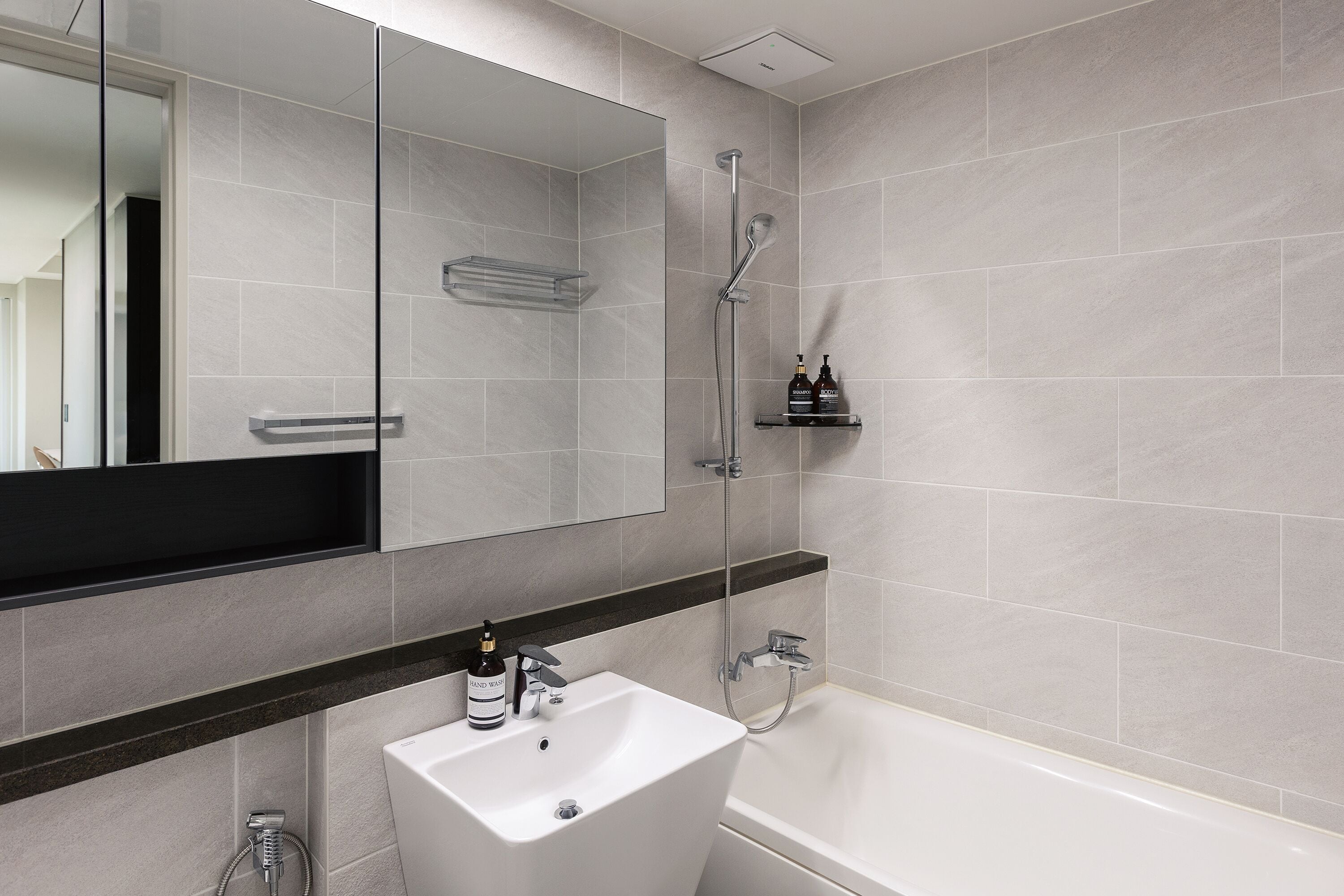 A modern bathroom with a large mirror, a white sink, a bathtub, and a shower.