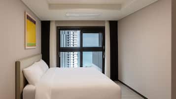 Una habitación de hotel con cama, ventana con vistas a edificios y una lámpara en el techo.