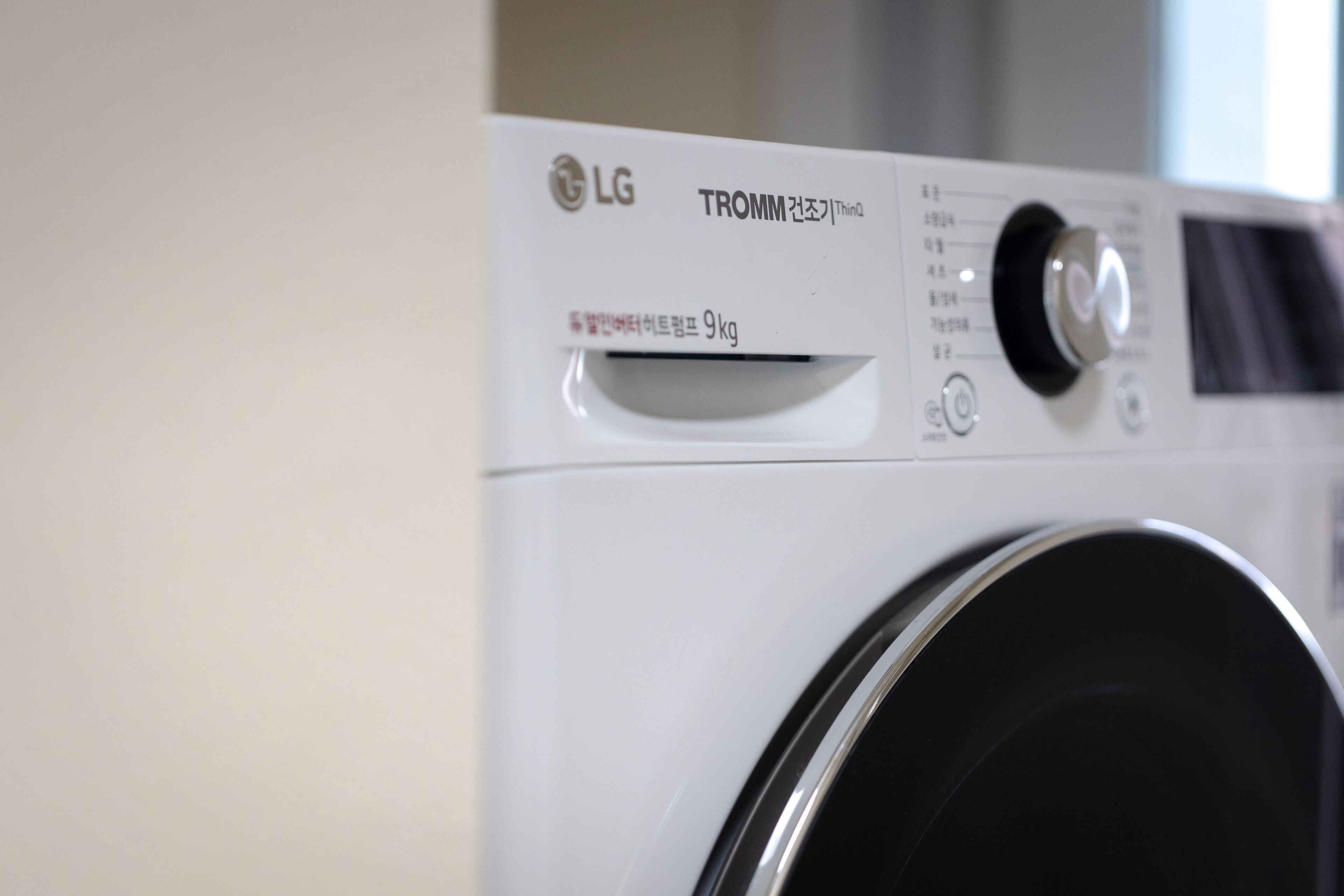 A white LG TROMM 9kg front-loading washing machine with a control panel and a black door.