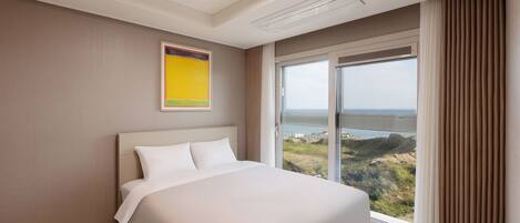 A modern hotel room with a large bed, a view of the landscape through a window, and a ceiling light.