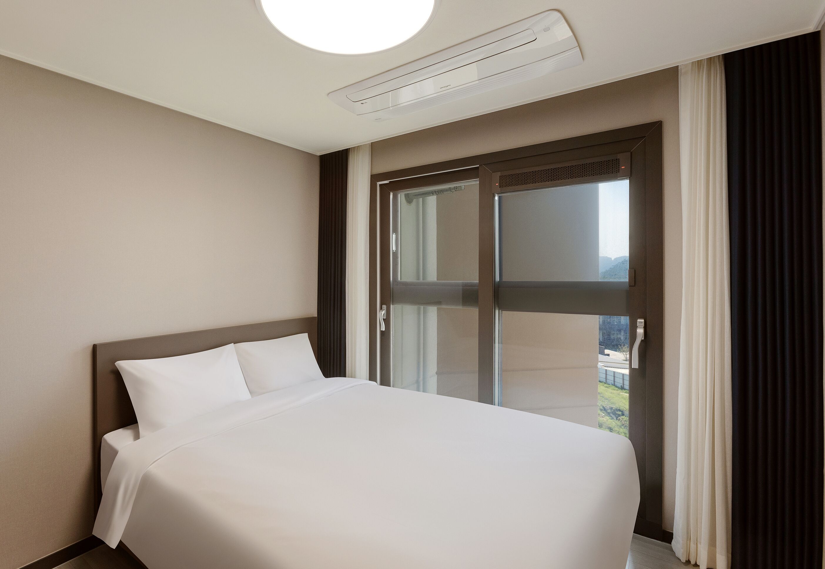 A hotel room with a large bed, a sliding glass door to the outside, and a ceiling-mounted air conditioning unit.