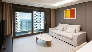 A modern living room with a white sofa, a round coffee table, and a large window offering a view of a building and the sky. - NewCZ Osiria Residence (Busan)