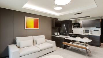 A modern living room with a sofa, a dining table, and a kitchen area with dark cabinetry and a stainless steel refrigerator.