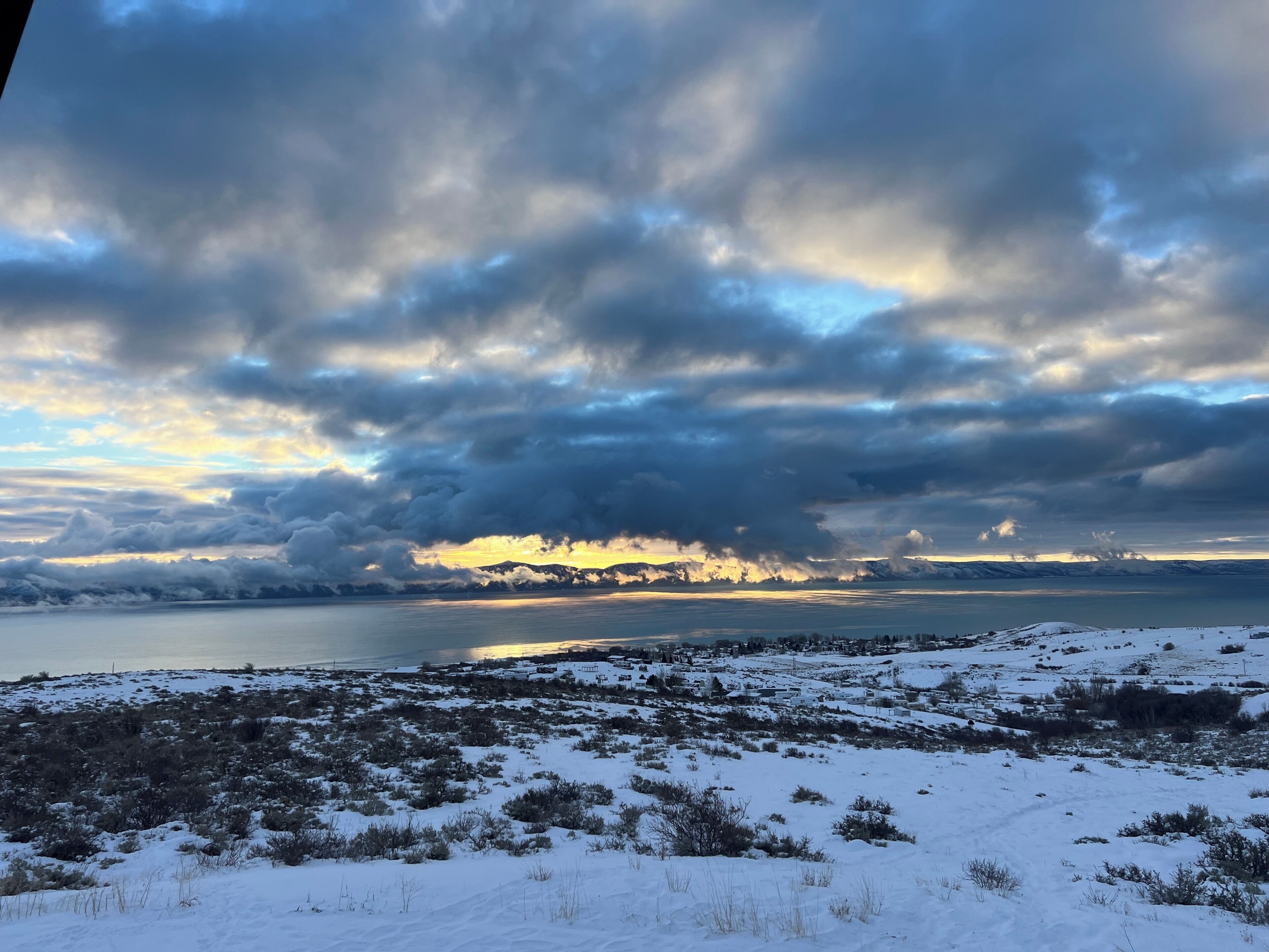 Eine verschneite Landschaft mit einem Gewässer und Bergen im Hintergrund.