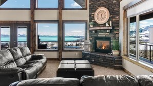 A cozy living room with a fireplace, leather sofa, and large windows offering a view of a snowy landscape. - Spectacular views of Bear Lake in a spacious private retreat on nearly 6 acres! (Fish Haven)