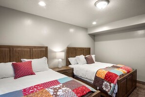 A hotel room with two beds, each with a wooden headboard, white bedding, and a colorful quilt. There is a nightstand with a lamp between the beds. - Spectacular views of Bear Lake in a spacious private retreat on nearly 6 acres! (Fish Haven)