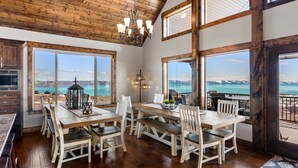A spacious dining area with a wooden table and chairs, large windows offering a view of a lake and mountains, and a chandelier hanging from the ceiling. - Spectacular views of Bear Lake in a spacious private retreat on nearly 6 acres! (Fish Haven)