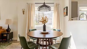 A dining area with a round table, six chairs, a vase with flowers, and a pendant light. - Quiet 2BR cottage, King Bed, Fire, <1 mi to Sugar (Avery County)