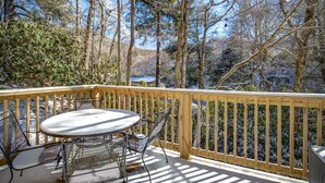 A wooden deck with a metal table and chairs, overlooking a forested area. - Quiet 2BR cottage, King Bed, Fire, <1 mi to Sugar (Avery County)
