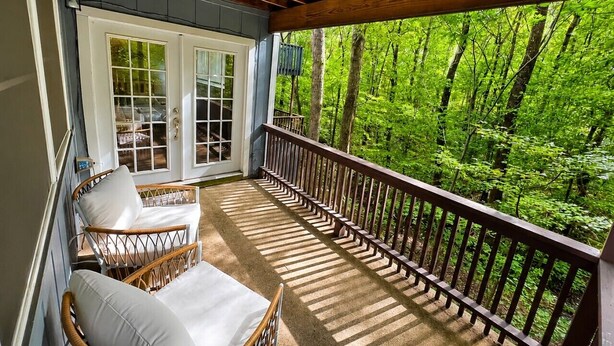 Eine überdachte Veranda mit Korbstühlen und Blick auf einen Wald.