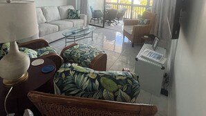 Un salon avec un canapé, une table basse et une lampe. On peut voir l’extérieur à travers une porte vitrée.