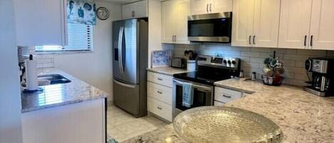 A modern kitchen with white cabinets, stainless steel appliances, and a granite countertop.