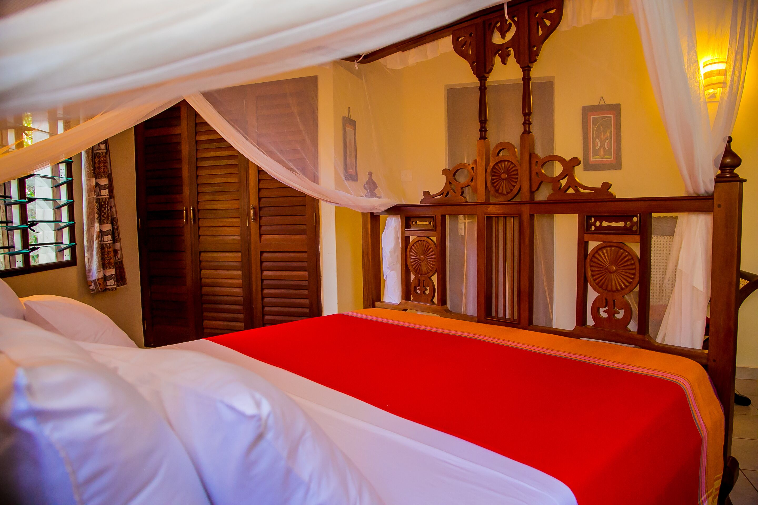 A bed with a red bedspread, wooden headboard, and white curtains.