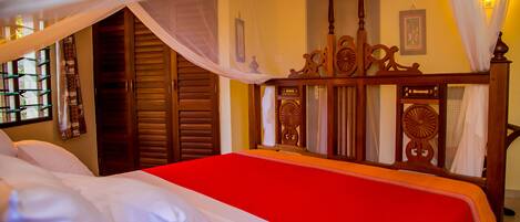 A bed with a red bedspread, wooden headboard, and white curtains.