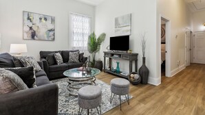A modern living room with a sofa set, a glass coffee table, and a flat-screen TV.