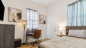 A bedroom with a bed, desk, chair, and artwork on the walls.