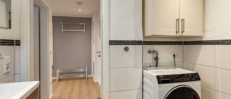 A laundry room with a front-loading washer and dryer, a towel rack, and a tiled backsplash.