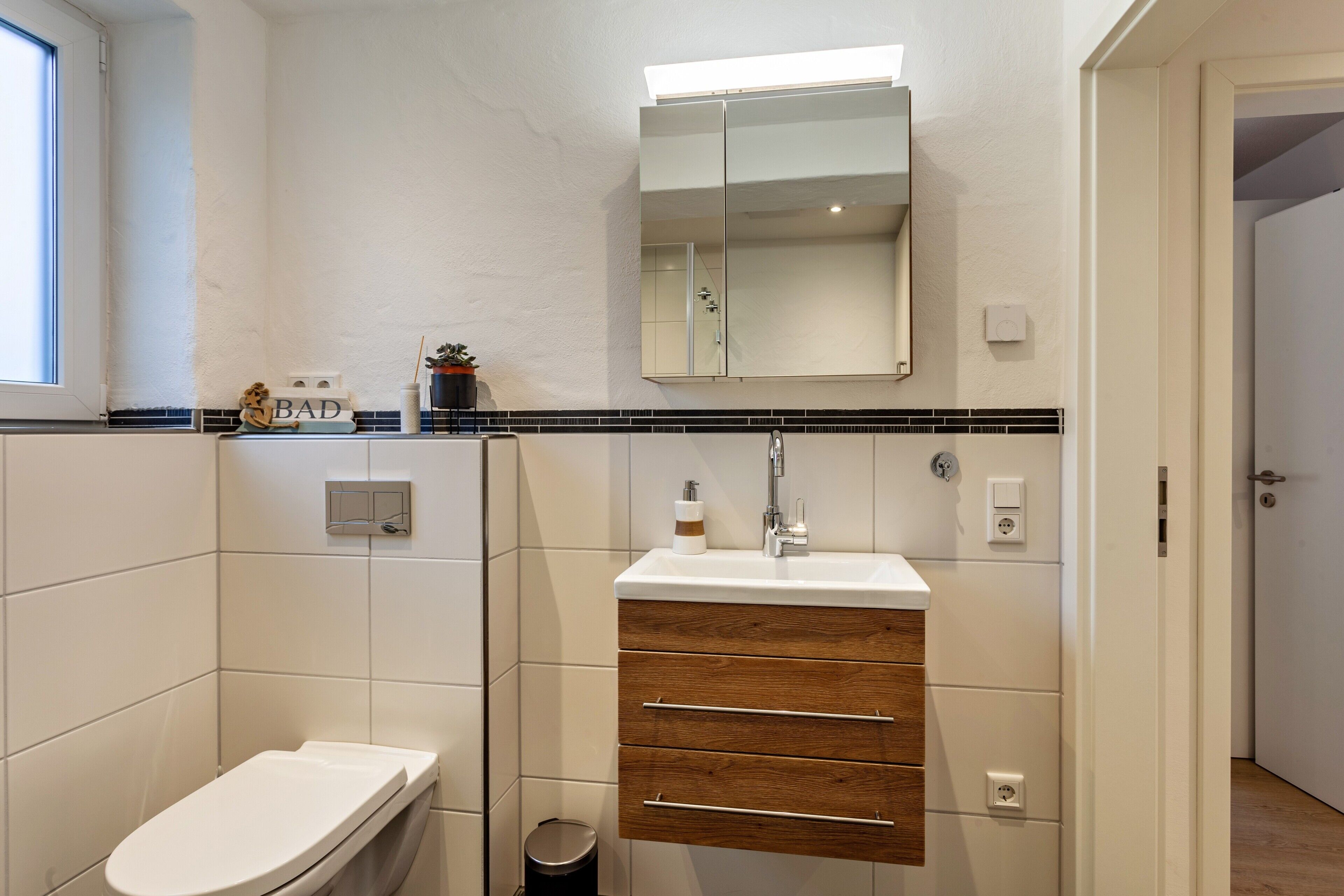 Ein Badezimmer mit Toilette, Waschbecken mit Spiegel und einem Schrank mit Schubladen.