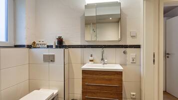 Ein Badezimmer mit Toilette, Waschbecken mit Spiegel und einem Schrank mit Schubladen.
